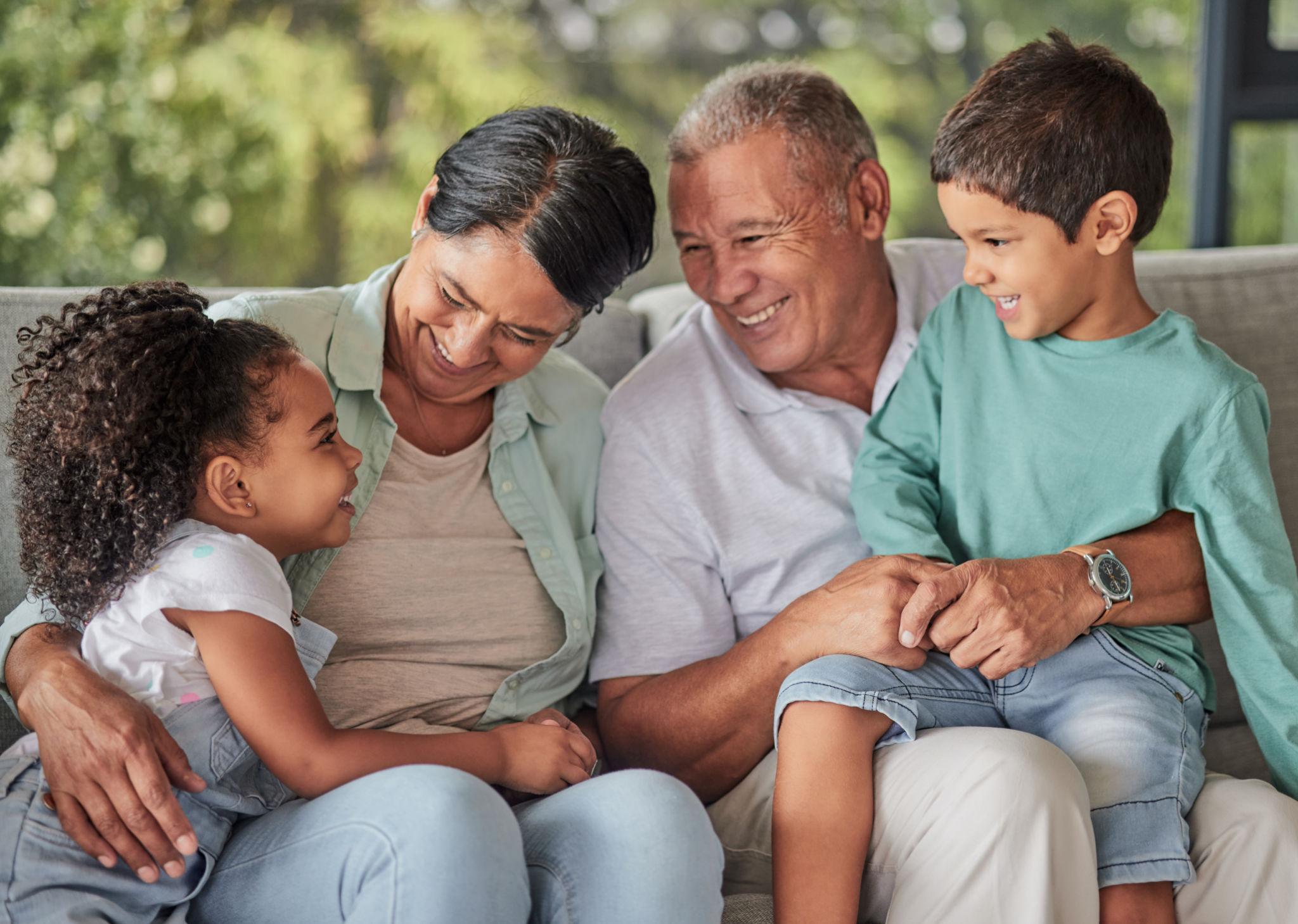 A multigenerational family sits close together on a couch outdoors, smiling and sharing a warm moment.
