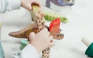 Child hands assembling a paper dinosaur puppet with a long neck during a craft activity at a table